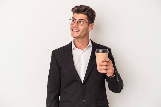 Giovane uomo caucasico di affari che tiene caffè da asporto isolato su sfondo bianco sognando di raggiungere obiettivi e scopi