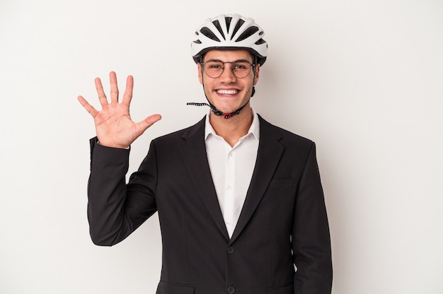 Giovane uomo caucasico di affari che tiene il casco della bici isolato su fondo bianco sorridente allegro che mostra il numero cinque con le dita.