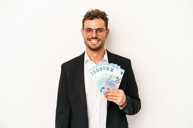 Giovane uomo caucasico di affari che tiene le banconote isolate su fondo bianco felice, sorridente e allegro.