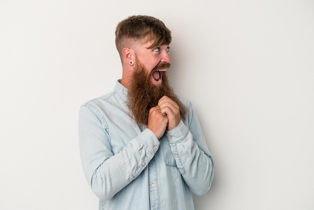 Giovane uomo caucasico di zenzero con barba lunga isolato su sfondo bianco che prega per fortuna, stupito e apre la bocca guardando in avanti.