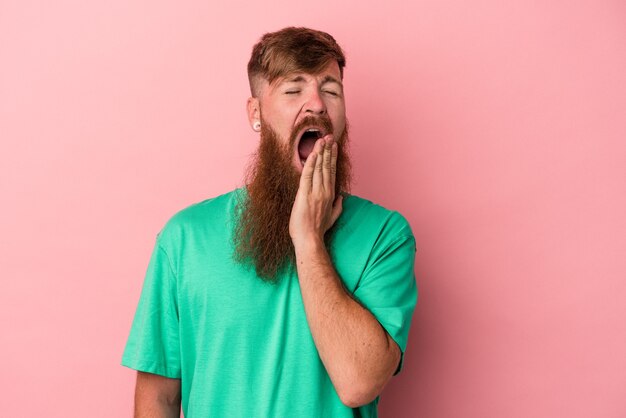 Giovane uomo caucasico di zenzero con barba lunga isolato su sfondo rosa che sbadiglia mostrando un gesto stanco che copre la bocca con la mano.