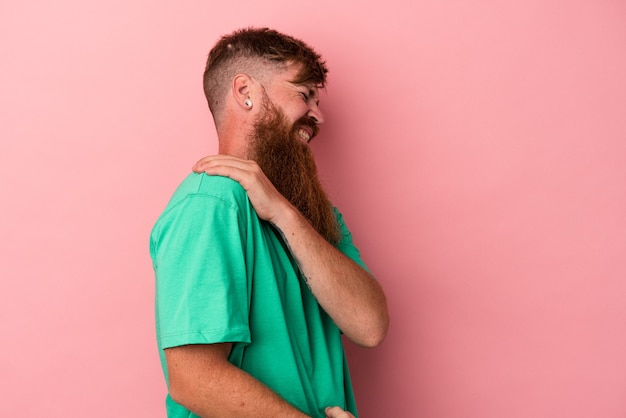 Giovane uomo caucasico di zenzero con barba lunga isolato su sfondo rosa con dolore alla spalla.