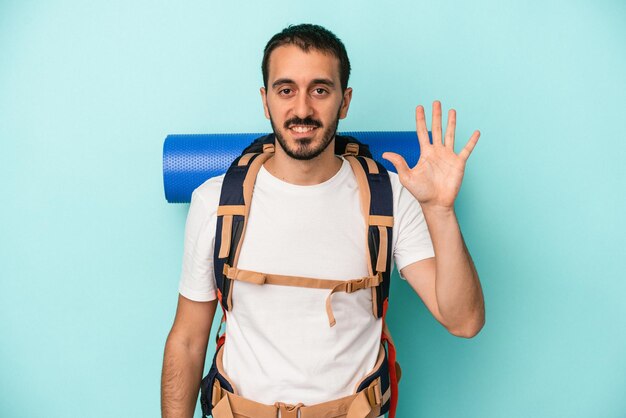 Giovane uomo caucasico escursionista isolato su sfondo blu sorridente allegro che mostra il numero cinque con le dita.