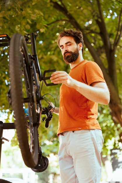 Giovane uomo caucasico in forma che ispeziona una bicicletta danneggiata nel cortile di casa pronto a riparare su un banco di riparazione professionale Ciclista maschio sportivo dedicato fuori a riparare la sua bicicletta moderna utilizzando strumenti specializzati