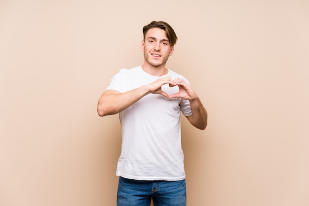 Giovane uomo caucasico in posa isolato sorridente e mostrando una forma di cuore con le mani.