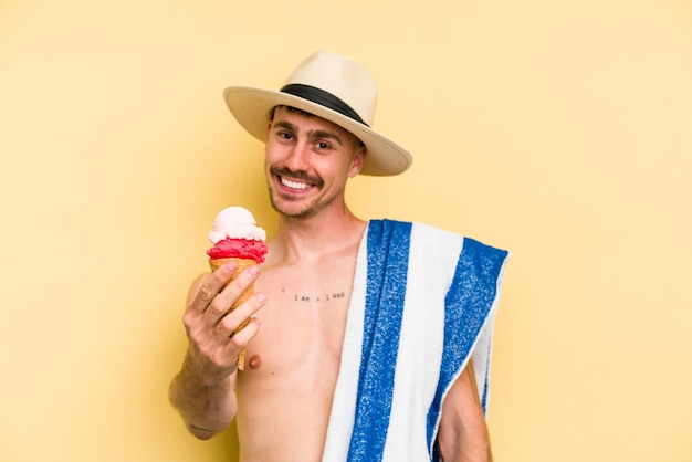 Giovane uomo caucasico in possesso di un gelato isolato su sfondo giallo