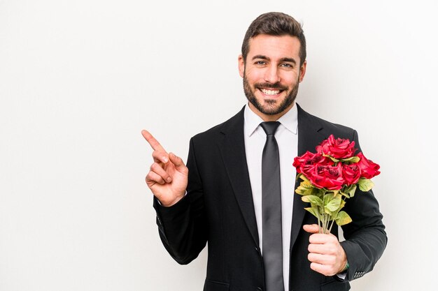 Giovane uomo caucasico in possesso di un mazzo di fiori isolati su sfondo bianco sorridente e indicando da parte mostrando qualcosa in uno spazio vuoto