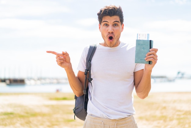 Giovane uomo caucasico in possesso di un passaporto all'aperto sorpreso e indicando il lato