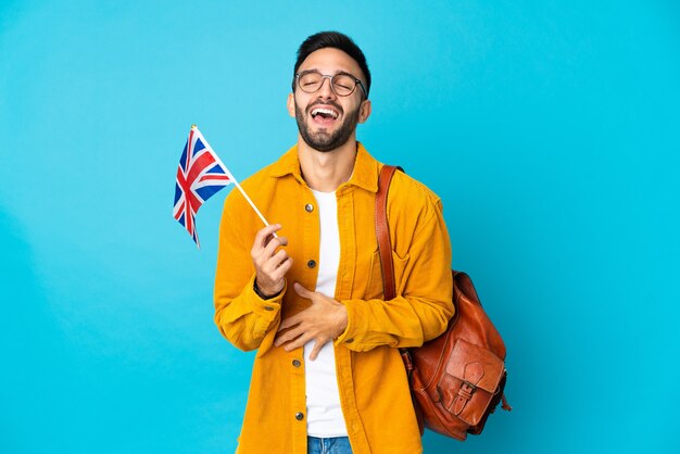 Giovane uomo caucasico in possesso di una bandiera del Regno Unito isolata su sfondo giallo sorridente molto