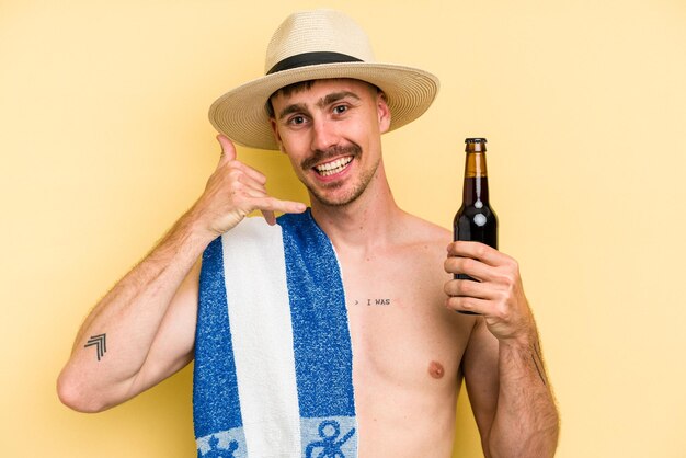 Giovane uomo caucasico in possesso di una birra isolata su sfondo giallo