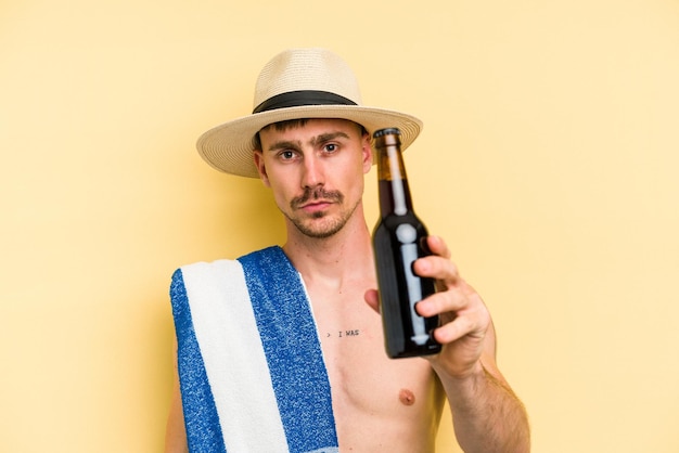 Giovane uomo caucasico in possesso di una birra isolata su sfondo giallo