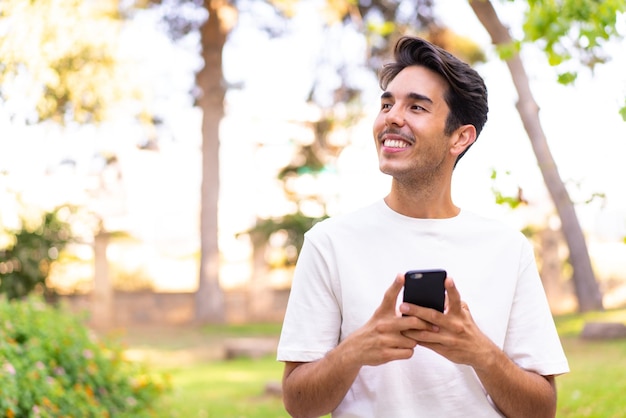 Giovane uomo caucasico in un parco utilizzando il telefono cellulare e alzando lo sguardo