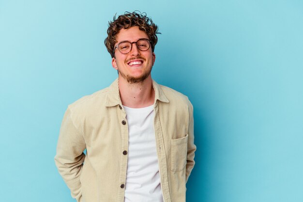 Giovane uomo caucasico indossando occhiali da vista isolati su sfondo blu felice, sorridente e allegro.