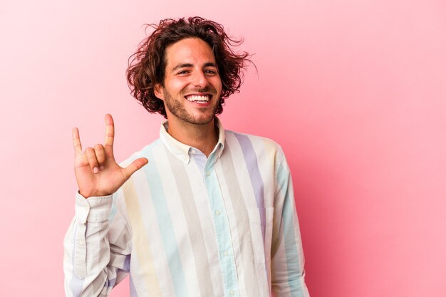 Giovane uomo caucasico isolato su bakcground rosa che mostra un gesto di corna come un concetto di rivoluzione.