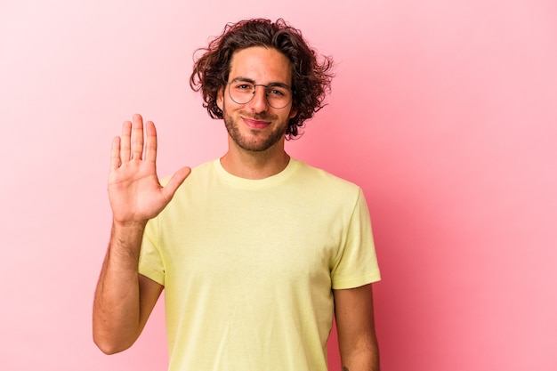 Giovane uomo caucasico isolato su bakcground rosa sorridente allegro che mostra il numero cinque con le dita.