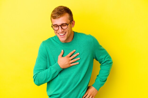 Giovane uomo caucasico isolato su giallo che ride mantenendo le mani sul cuore, il concetto di felicità.