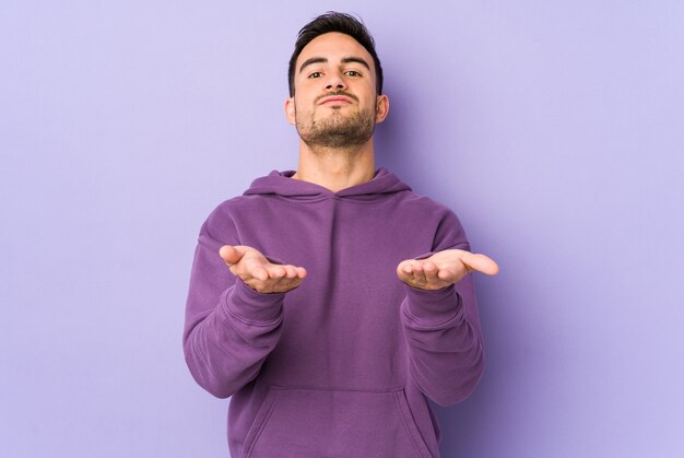 Giovane uomo caucasico isolato su labbra pieghevoli viola e tenendo i palmi delle mani per inviare un bacio d'aria.