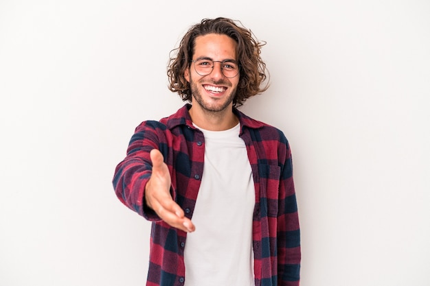 Giovane uomo caucasico isolato su priorità bassa bianca che allunga la mano alla macchina fotografica nel gesto di saluto.