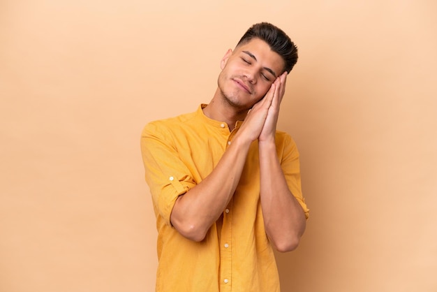 Giovane uomo caucasico isolato su sfondo beige che fa il gesto del sonno in un'espressione adorabile