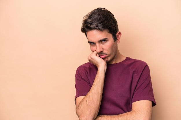 Giovane uomo caucasico isolato su sfondo beige che si sente triste e pensieroso guardando lo spazio della copia