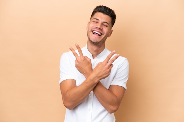 Giovane uomo caucasico isolato su sfondo beige sorridente e mostrando il segno di vittoria