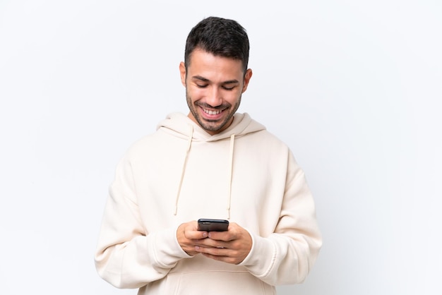 Giovane uomo caucasico isolato su sfondo bianco che manda un messaggio con il cellulare