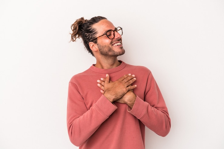 Foto giovane uomo caucasico isolato su sfondo bianco che ride tenendo le mani sul cuore, concetto di felicità.
