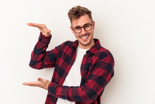 Giovane uomo caucasico isolato su sfondo bianco che tiene qualcosa di piccolo con l'indice, sorridente e fiducioso.