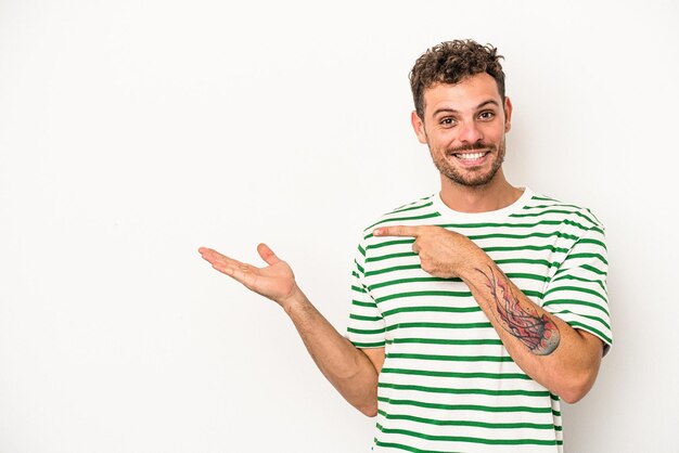 Giovane uomo caucasico isolato su sfondo bianco eccitato tenendo uno spazio copia sul palmo.