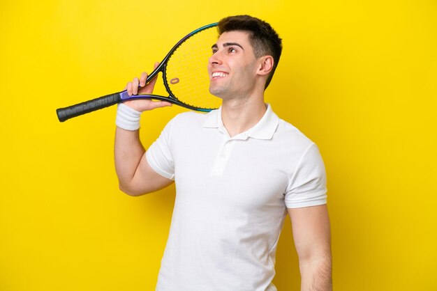 Giovane uomo caucasico isolato su sfondo bianco giocando a tennis e alzando lo sguardo