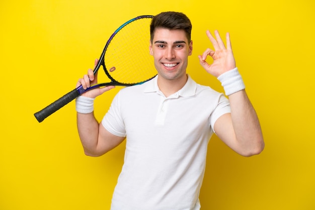 Giovane uomo caucasico isolato su sfondo bianco giocando a tennis e facendo segno OK