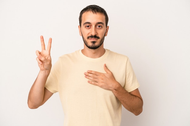 Giovane uomo caucasico isolato su sfondo bianco prestando giuramento, mettendo la mano sul petto.