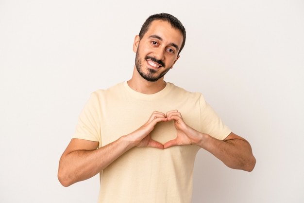 Giovane uomo caucasico isolato su sfondo bianco sorridente e mostrando una forma di cuore con le mani.