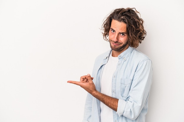 Giovane uomo caucasico isolato su sfondo bianco sorridente e rivolto da parte, mostrando qualcosa in uno spazio vuoto.