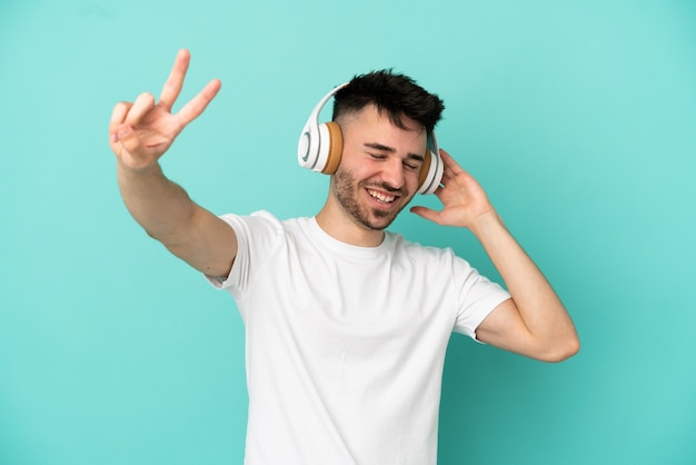 Giovane uomo caucasico isolato su sfondo blu ascoltando musica e cantando