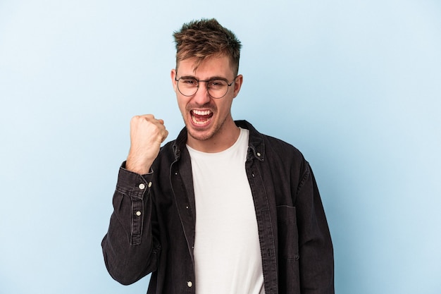 Giovane uomo caucasico isolato su sfondo blu che celebra una vittoria, passione ed entusiasmo, espressione felice.