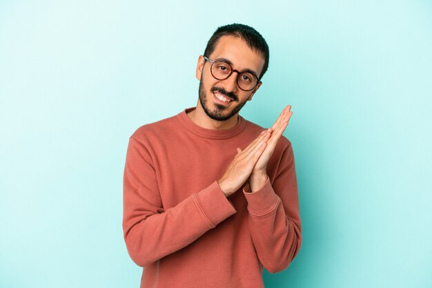 Giovane uomo caucasico isolato su sfondo blu che si sente energico e a suo agio, sfregandosi le mani fiduciose.