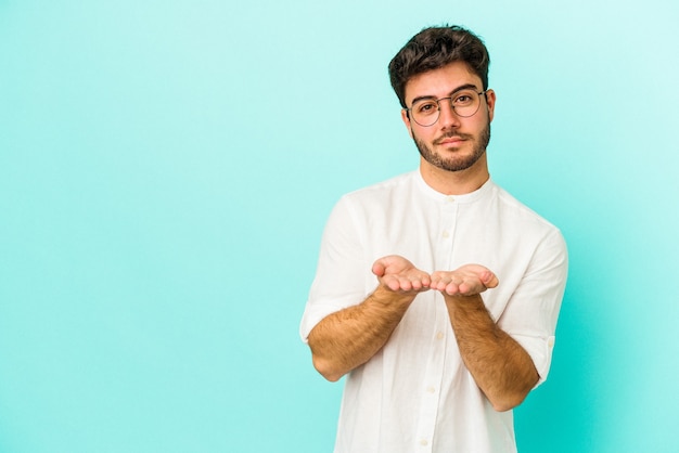 Giovane uomo caucasico isolato su sfondo blu piegando le labbra e tenendo i palmi delle mani per inviare un bacio d'aria.