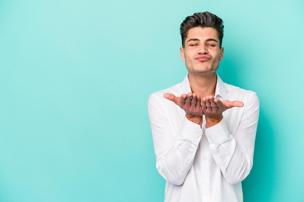 Giovane uomo caucasico isolato su sfondo blu piegando le labbra e tenendo i palmi delle mani per inviare un bacio d'aria.