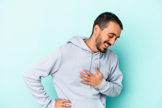 Giovane uomo caucasico isolato su sfondo blu ridendo tenendo le mani sul concetto di felicità del cuore