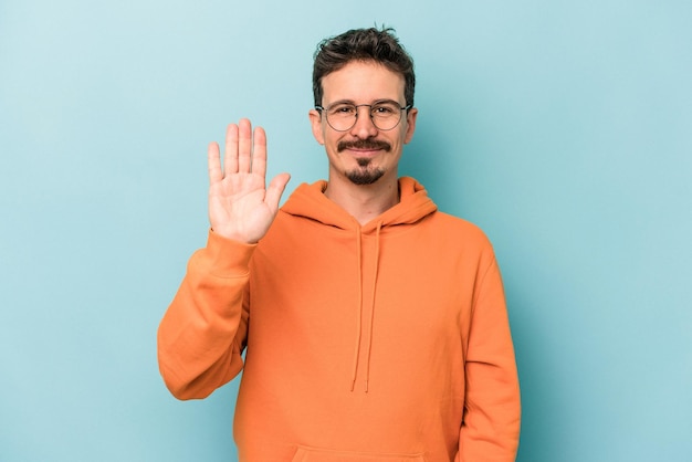 Giovane uomo caucasico isolato su sfondo blu sorridente allegro che mostra il numero cinque con le dita.