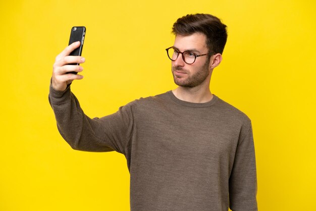 Giovane uomo caucasico isolato su sfondo giallo che fa un selfie