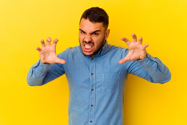 Giovane uomo caucasico isolato su sfondo giallo che mostra gli artigli imitando un gatto, gesto aggressivo.