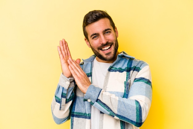 Giovane uomo caucasico isolato su sfondo giallo che si sente energico e a proprio agio strofinandosi le mani fiducioso