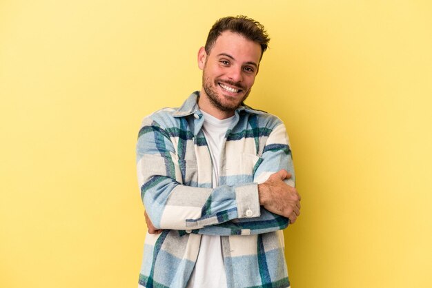 Giovane uomo caucasico isolato su sfondo giallo che si sente sicuro, incrociando le braccia con determinazione.