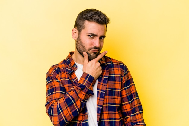 Giovane uomo caucasico isolato su sfondo giallo contemplando la pianificazione di una strategia pensando al modo di fare affari