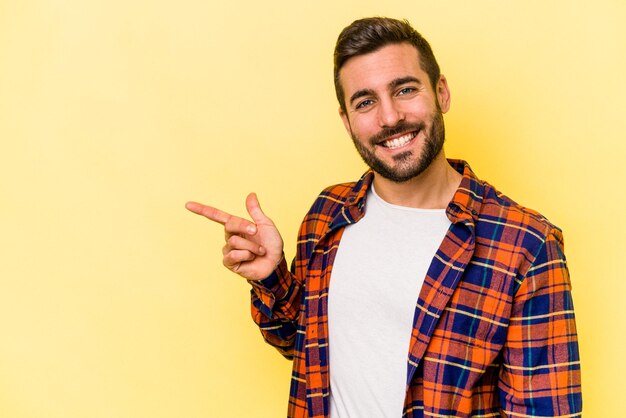 Giovane uomo caucasico isolato su sfondo giallo sorridente allegramente indicando con l'indice lontano