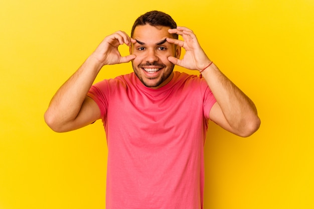 Giovane uomo caucasico isolato su sfondo giallo tenendo gli occhi aperti per trovare un'opportunità di successo.