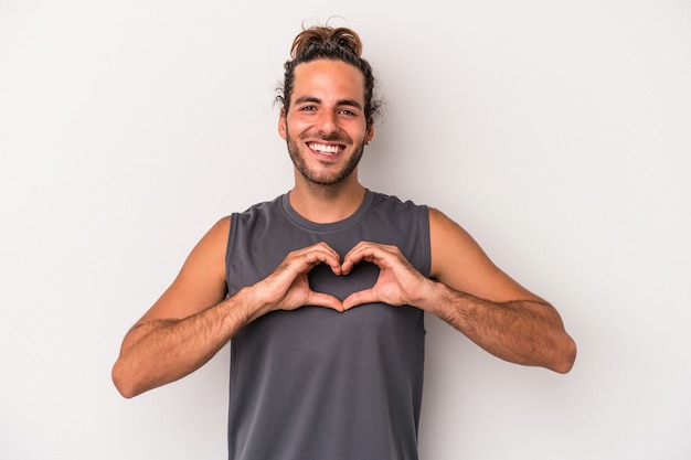 Giovane uomo caucasico isolato su sfondo grigio sorridente e mostrando una forma di cuore con le mani.