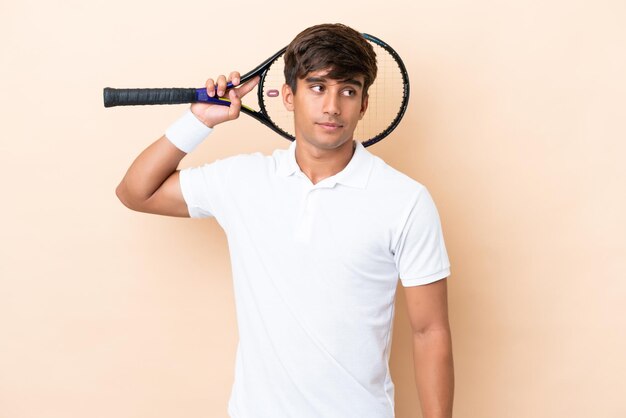 Giovane uomo caucasico isolato su sfondo ocra giocando a tennis